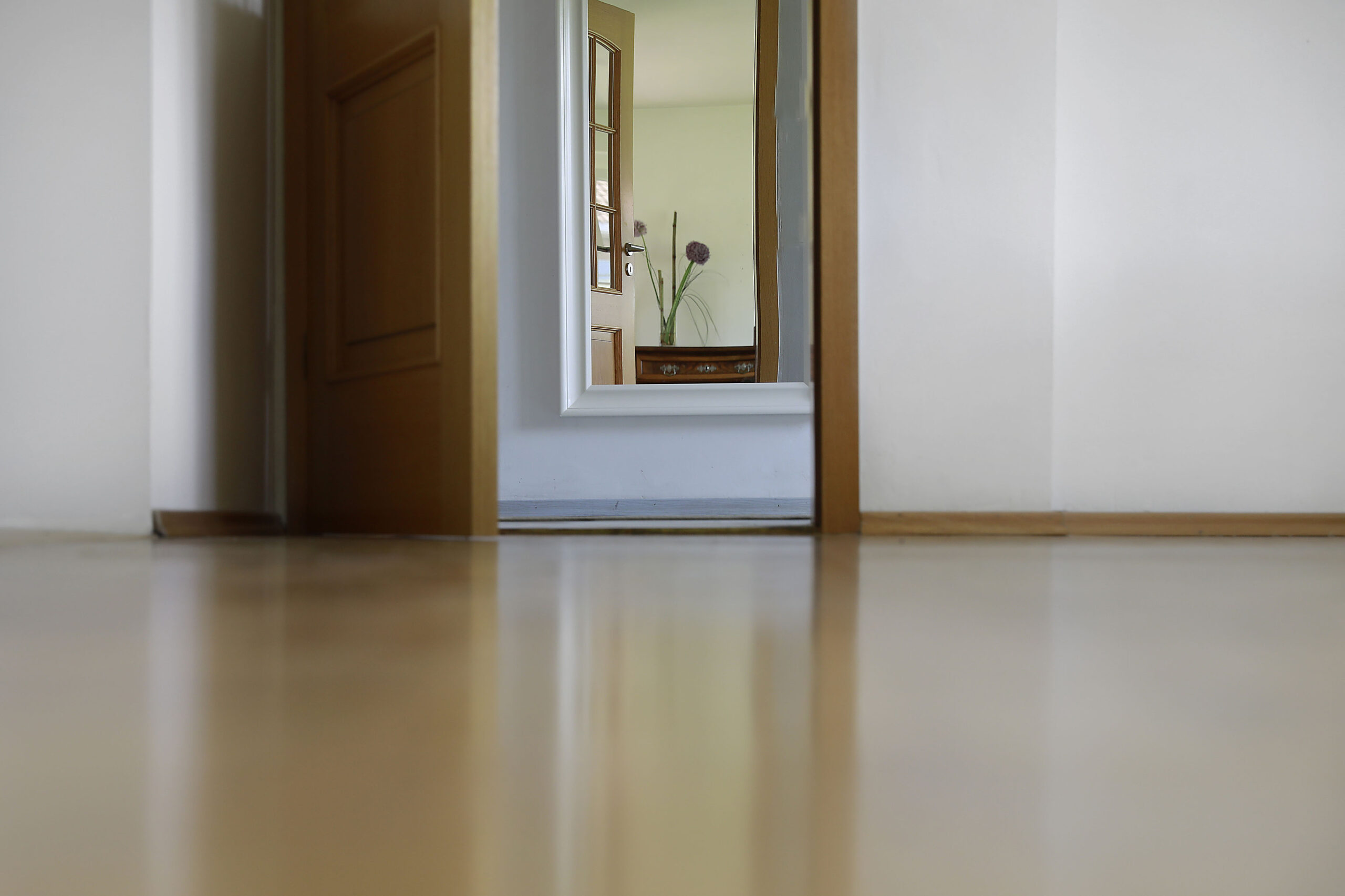 Blick über den hellen Holzboden durch eine offene Tür in den Flur des Ferienhauses Falkenhaus Scheidegg