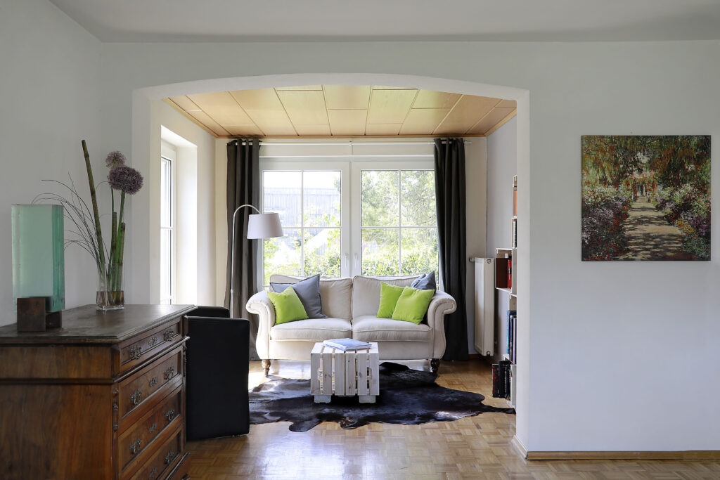 Wohnzimmer mit Rundbogen, Sofa vor dem Fenster und Blick in den Garten im Ferienhaus Falkenhaus Scheidegg